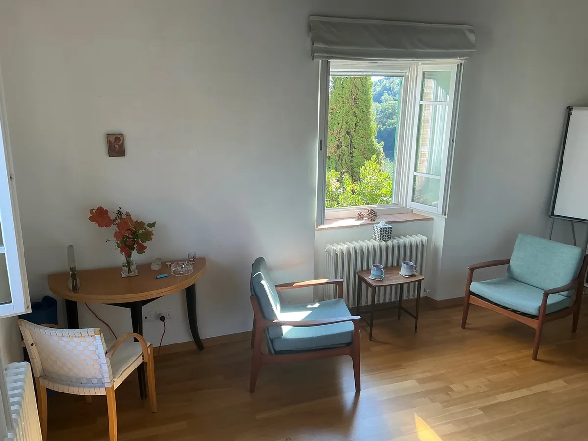 Zimmer mit Sesseln, Tisch und Blumen am offenen Fenster