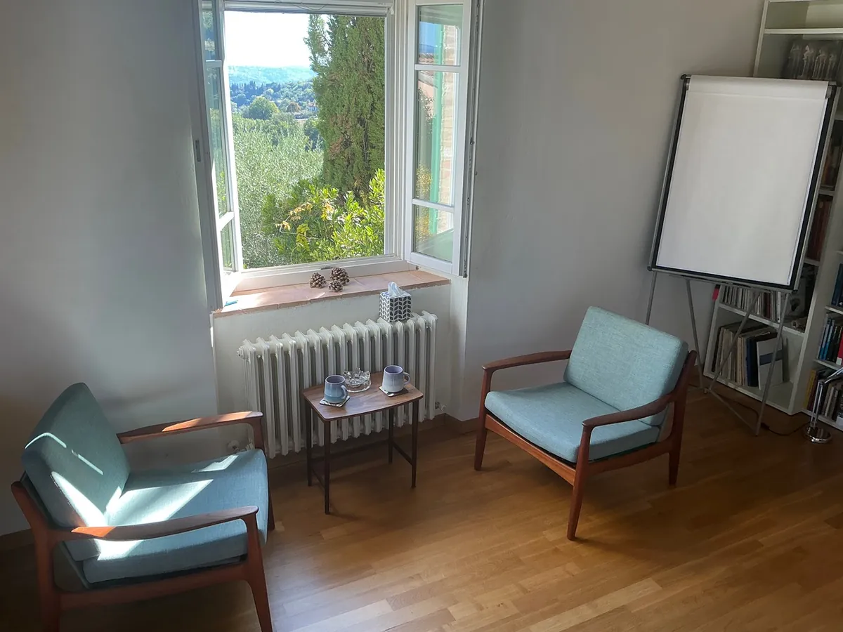 Heller Raum mit zwei Sesseln, einem Tisch und Blick aus dem Fenster ins Grüne